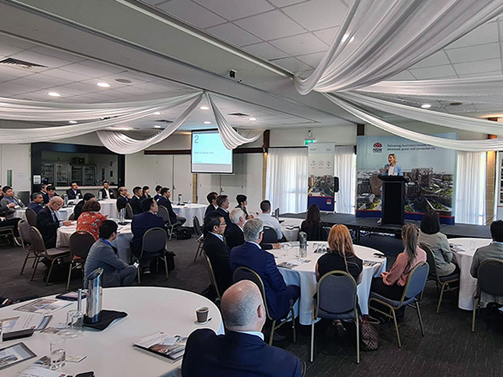 Business people sitting at conference tables listening to a presenter on stage