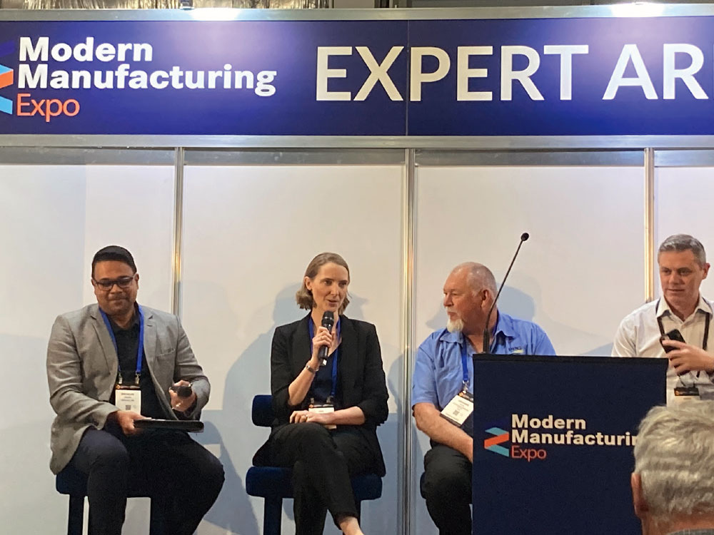 Three men and one woman engaging in a panel discussion on stage at a conference