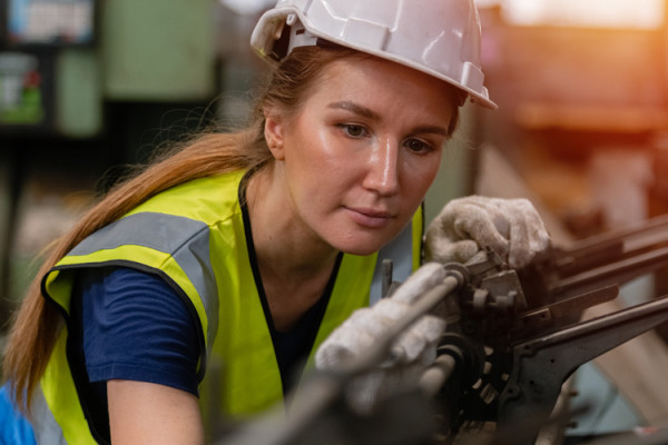 A female engineer, wearing a had hat and high-vis vest, working at a lathe