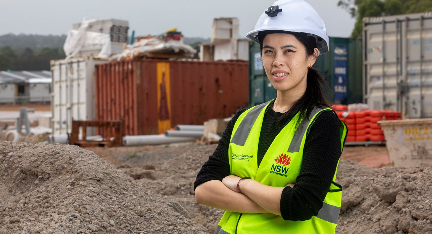 A woman standing with her arms folded, on a construction site wearing a hard hat and high vis vest.