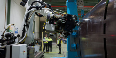 Three workers speaking near a robotic arm located in a manufacturing facility